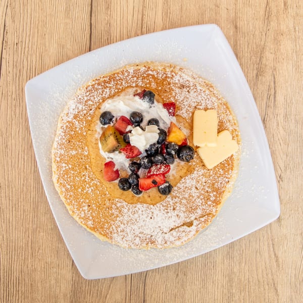 Overhead view of a pancake with whipped cream, blueberries, strawberries, kiwi, and butter.
