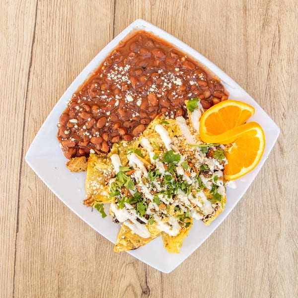 Chilaquiles with beans, cheese, cilantro, and sour cream, garnished with orange slices.