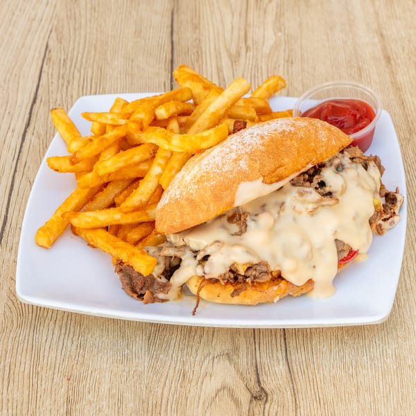 Cheesesteak sandwich with melted cheese, onions, and peppers, served with golden fries and ketchup.