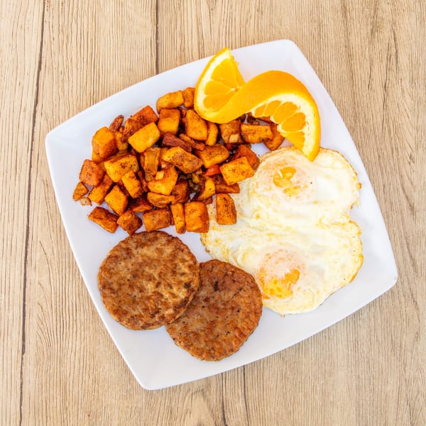 Breakfast plate with two fried eggs, two sausage patties, home fries, and orange slices.