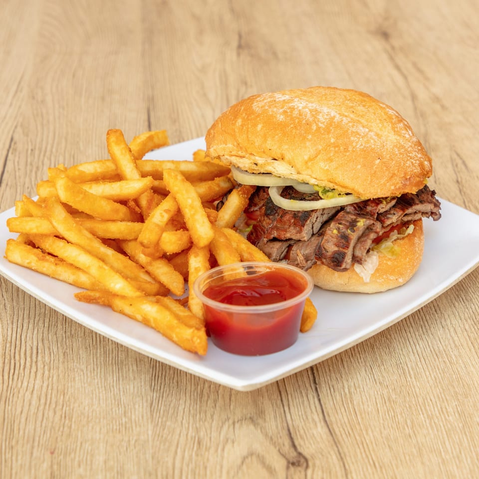 Grilled steak sandwich with onions and lettuce, served with golden french fries and ketchup.