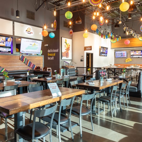 A vibrant, empty Mexican restaurant dining room with colorful decorations, wooden tables, and televisions.