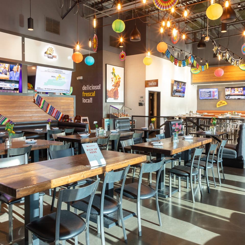 A vibrant, empty Mexican restaurant dining room with colorful decorations, wooden tables, and televisions.