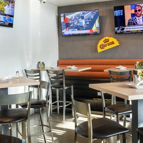 Restaurant interior with high-top tables, bar stools, an orange booth, and multiple TVs showing sports.