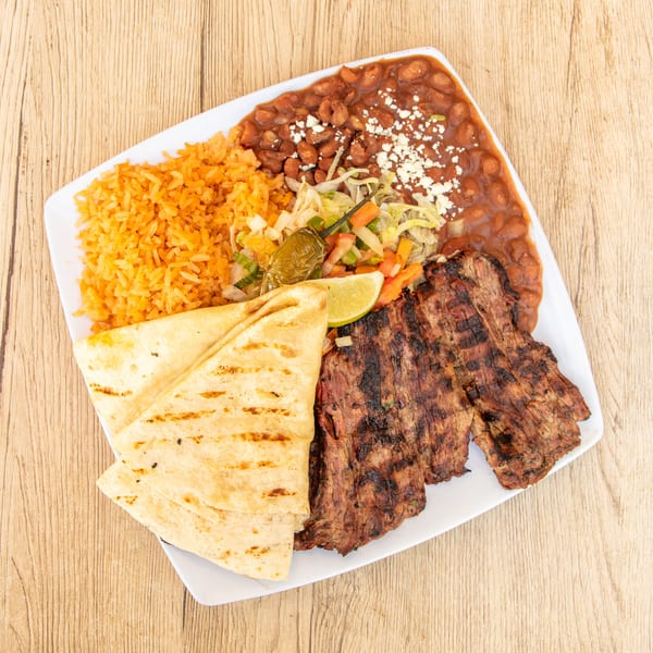 Grilled steak, rice, beans, salad, tortillas, and a lime wedge on a white plate.