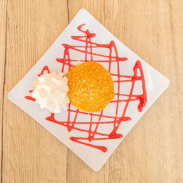 Fried ice cream dessert with whipped cream and strawberry syrup on a white square plate.