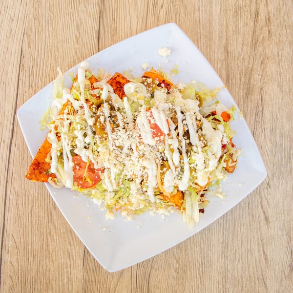 A plate of Mexican enchiladas topped with lettuce, tomatoes, sour cream, and crumbled cheese.