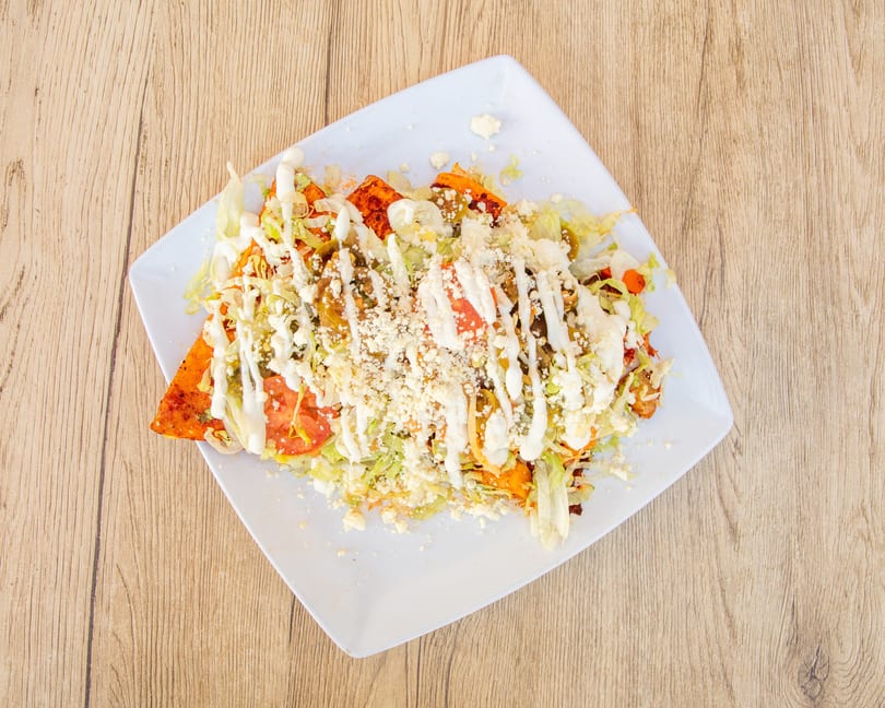 A plate of Mexican enchiladas topped with lettuce, tomatoes, sour cream, and crumbled cheese.