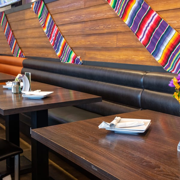 Restaurant interior with dark wooden tables, black and orange booths, and colorful striped fabric wall decor.