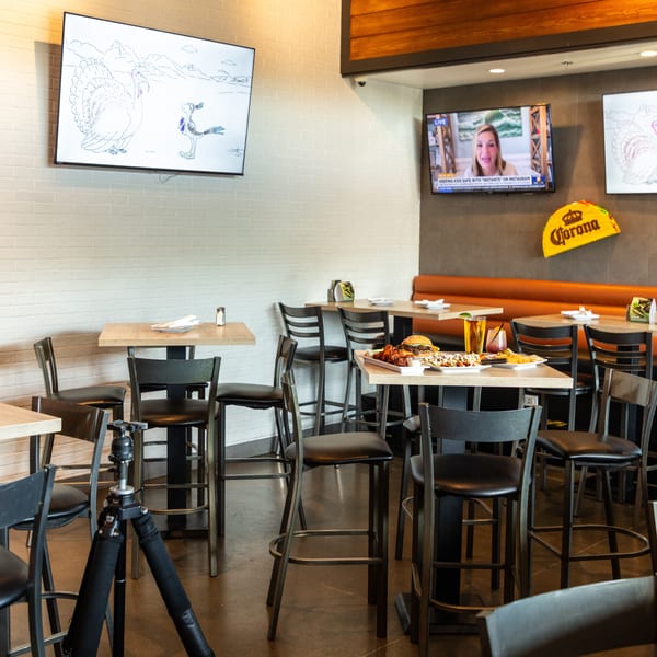 Restaurant interior with high-top tables, bar stools, a booth, and TVs showing news and cartoons.