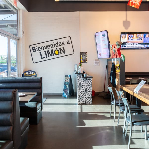 Interior of Limón restaurant with booths, tables, a welcome sign, and TVs on the walls.