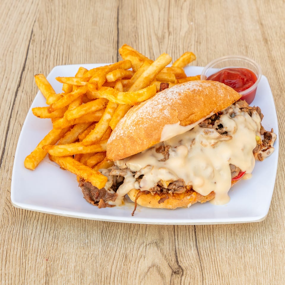 Cheesesteak sandwich with melted cheese, onions, and peppers, served with golden fries and ketchup.